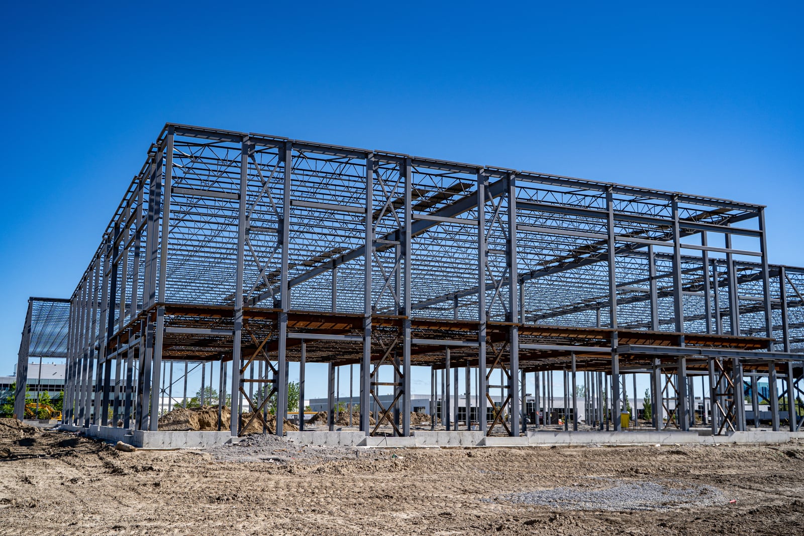 Steel frame of an industrial building under construction beneath a clear blue sky.
