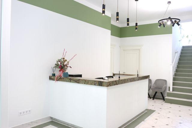 White clinic reception counter with a dark stone top, green wall accents and hanging lights.