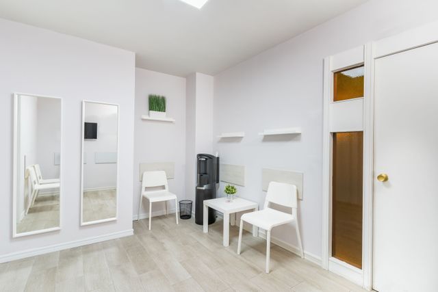 Bright waiting area with white chairs, a small table, tall mirrors and pale timber flooring.
