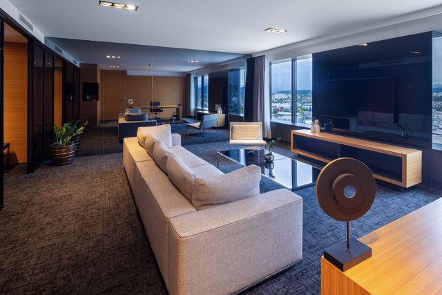 Hotel-suite living room with contemporary seating, blue-grey carpet and wide windows