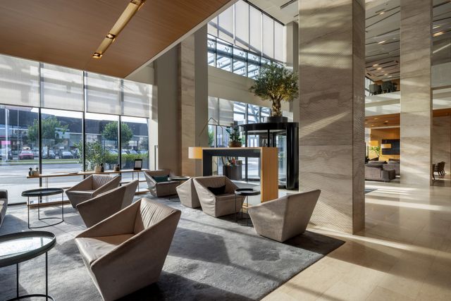 Double-height hotel lobby with modern armchairs, stone columns and large windows