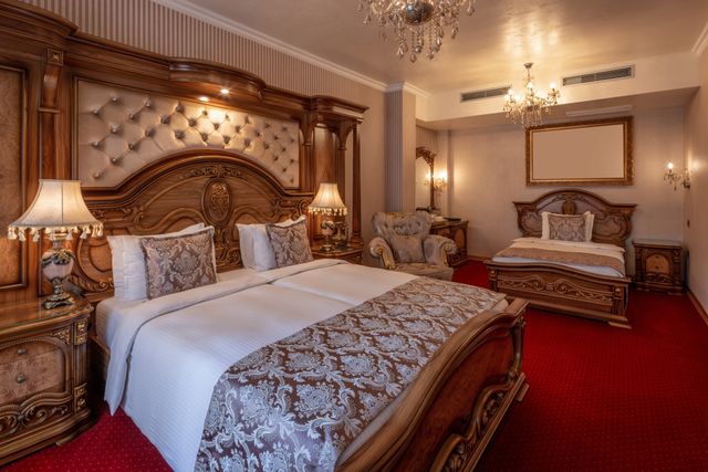 Classic hotel suite with ornate timber furniture, warm metallic details and large beds