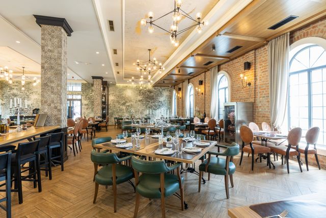 Restaurant with tall arched windows, chandeliers and textured brick-and-stone finishes