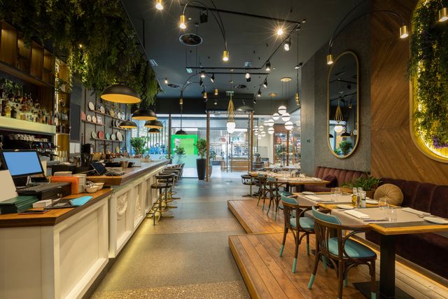 Restaurant with a long bar counter, dark ceiling and greenery across the interior