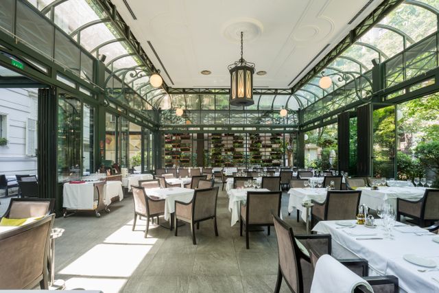 Restaurant terrace beneath a glazed roof with elegant dining furniture and natural light