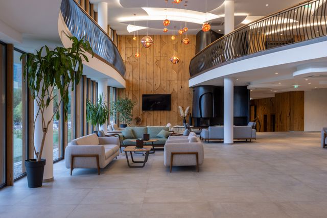 Double-height hotel lobby with a curved mezzanine, timber feature wall and neutral seating