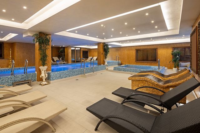 Hotel indoor spa-pool with mosaic walls, loungers and layered ceiling lighting