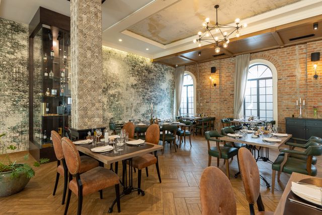 Restaurant dining area with timber tables, upholstered chairs, arched windows, patterned walls and decorative ceiling lighting.