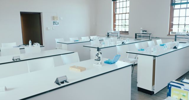 School science laboratory with rows of white workbenches, microscopes and large windows.