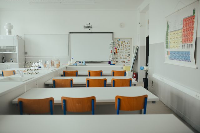 Science classroom with rows of desks, timber chairs, teaching boards and laboratory materials along a side counter.