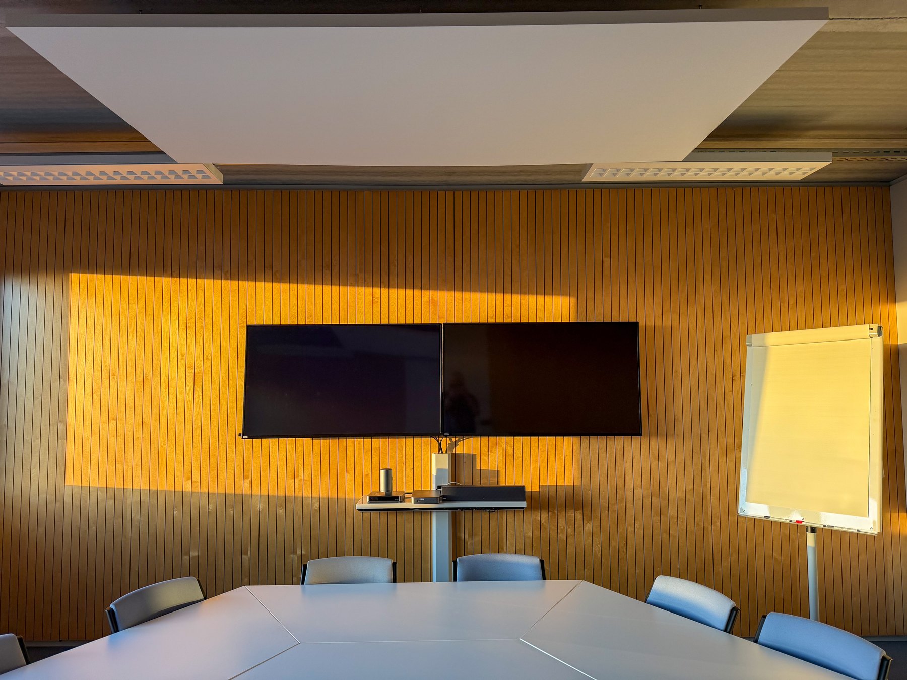Conference table facing twin displays on a timber feature wall.