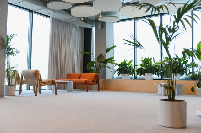 Office lounge with large windows, indoor plants and orange and neutral seating.