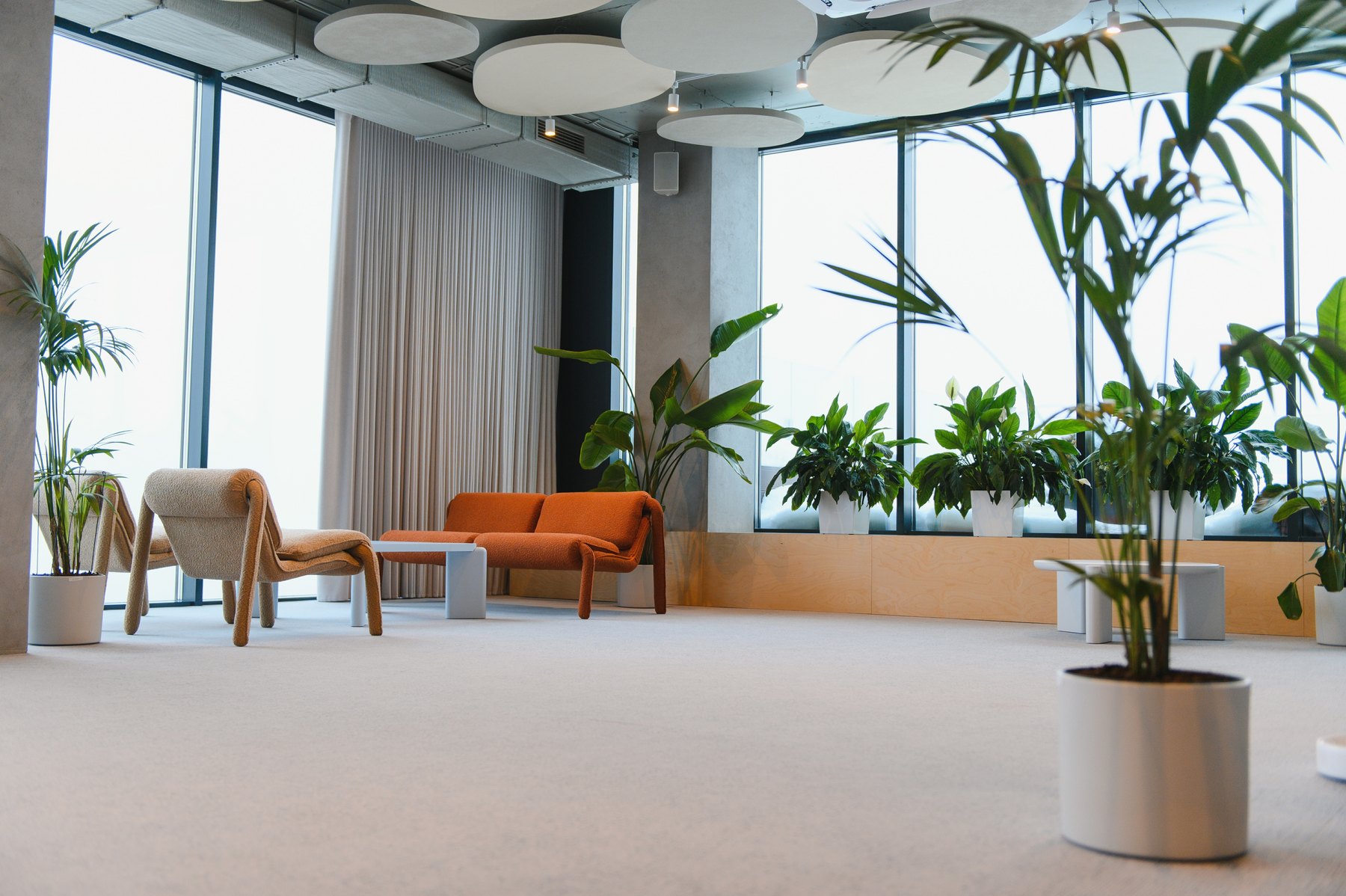 Office lounge with large windows, indoor plants and orange and neutral seating.