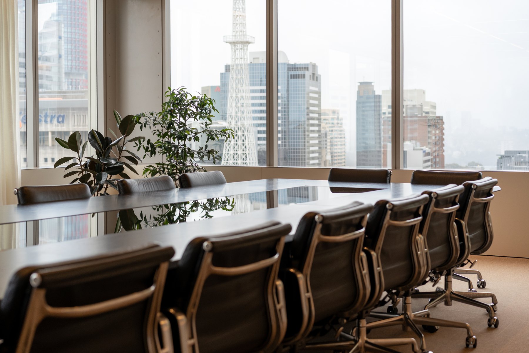 Long conference table with upholstered chairs beside full-height windows.