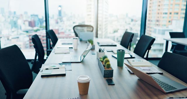 Meeting table with chairs, notebooks and small plants beside a city-facing window.