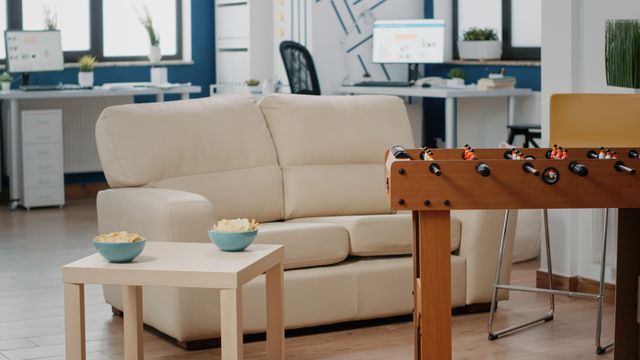 Office recreation corner with a cream sofa, coffee table and table football beside workstations.