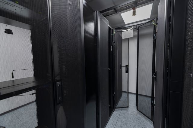 Narrow server-room aisle lined with dark mesh-fronted equipment cabinets under overhead lighting.