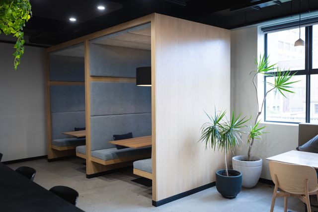 Timber-framed seating booths with grey upholstered panels beside a bright window and indoor plants.