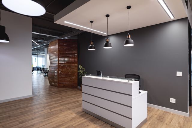 White reception counter against a charcoal wall with pendant lighting, timber flooring and a slatted screen.