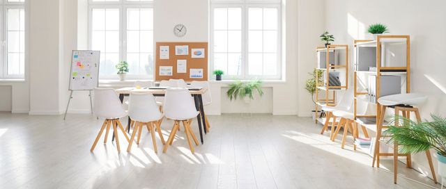 Small meeting area with white chairs, a timber table, presentation boards, open shelving and large windows.