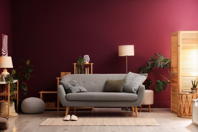 Grey sofa, plants and a timber room divider against a burgundy living-room wall.