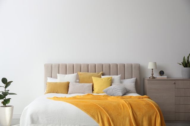Upholstered bed with yellow bedding, neutral headboard and simple bedside furniture.