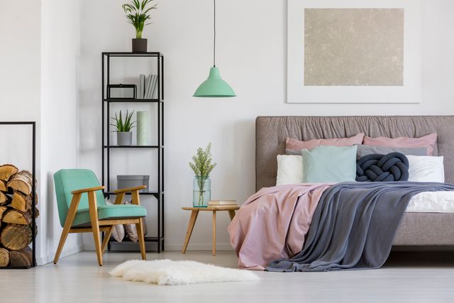 Bedroom with a pink and grey bed, mint-green pendant lamp, shelving and a timber chair.