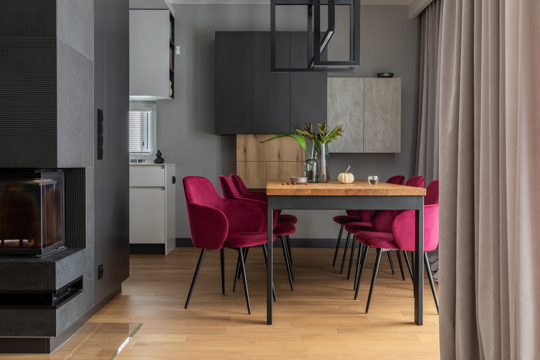 Timber dining table with burgundy velvet chairs against a dark feature wall.