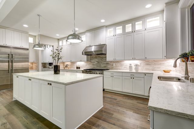 White shaker-style kitchen with an island, tiled backsplash and stainless-steel appliances.