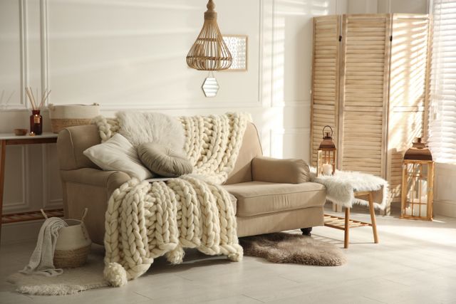 Beige sofa with cushions and a knitted throw, a woven pendant and timber room screen.