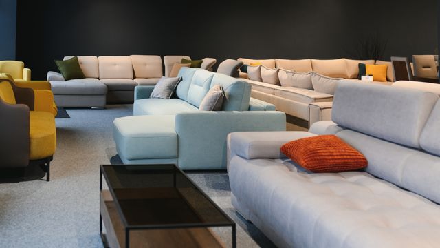 Furniture showroom with neutral and pastel sofas, occasional tables and cushions against a dark feature wall.