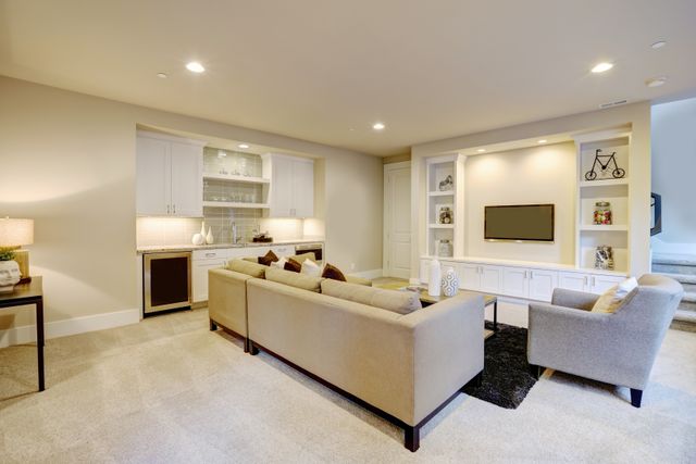 A residential entertainment room pairs a wet bar with a grey sectional sofa and a television area.