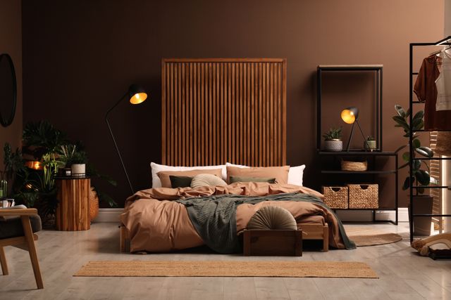 Brown walls, timber accents and layered bedding create a warm bedroom with a low upholstered bed.