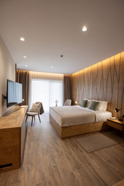White bedding contrasts with warm wood paneling in a bedroom opening toward a bright window.
