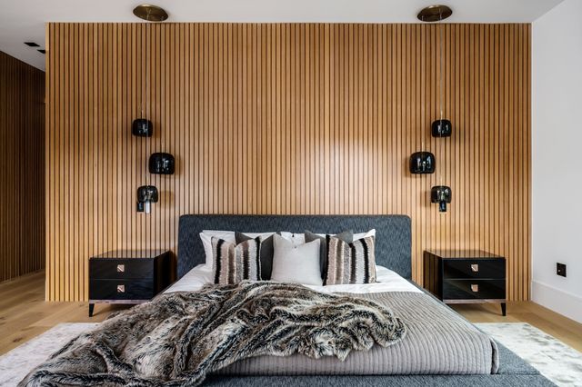 A grey bed sits against a vertical timber-slat wall beneath dark hanging bedside lights.