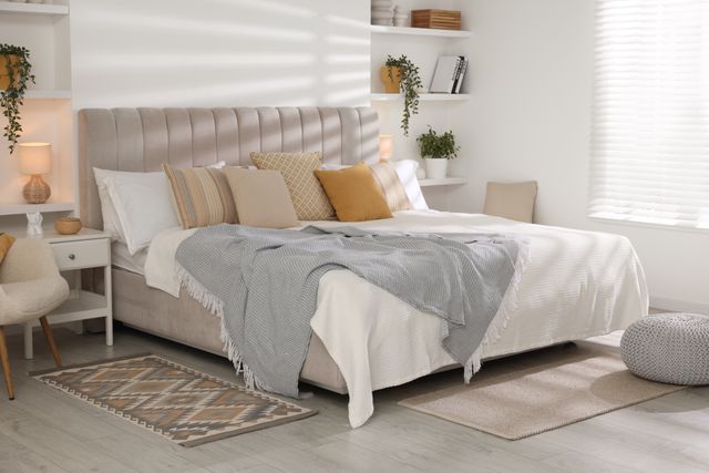A cream upholstered bed, pale textiles and a small accent cushion furnish a bright bedroom.