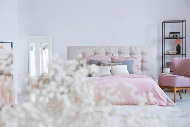 A padded bed with pastel pink bedding sits beside open shelving and a pink chair.