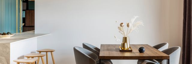 A rectangular wood dining table and grey chairs form a compact dining area beside a light kitchen counter.