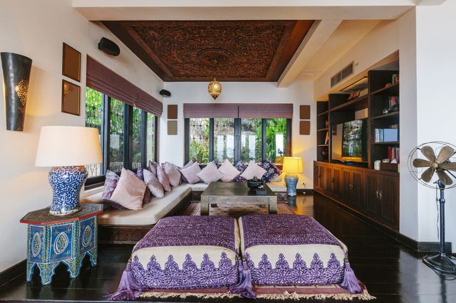 Cream sofas and dark timber furnishings fill a spacious living room with a carved ceiling and large windows.
