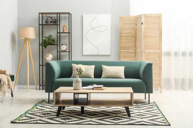 A green sofa, timber coffee table and folding screen are arranged against light walls with open shelving.