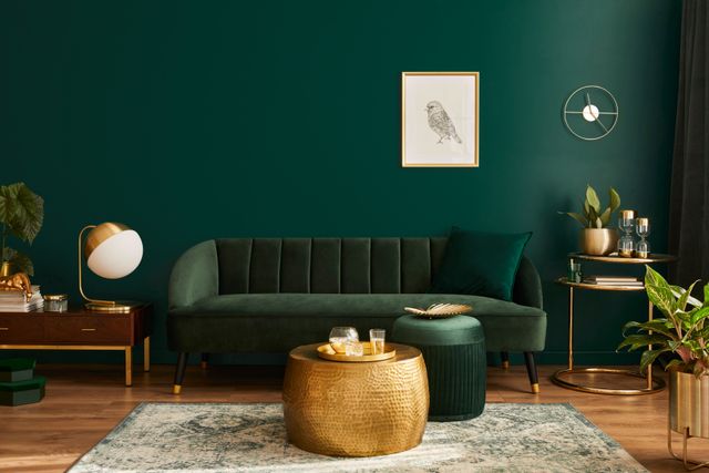 A green velvet sofa and matching wall are paired with gold-toned tables, lighting and decorative accessories.