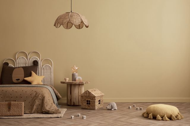 A woven bed, small toys and a petal-shaped pendant sit against a warm yellow wall.