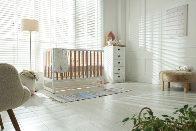 A timber-and-white crib and a small chest of drawers stand beside tall windows in a bright nursery.