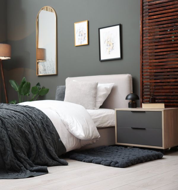A bed is paired with muted green walls, timber slats and simple furnishings in a teenager's room.