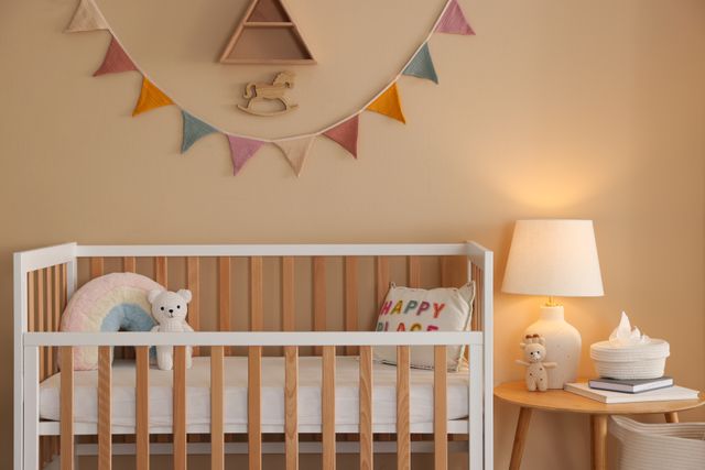 A crib, side table and lamp create a softly furnished nursery in warm neutral tones.