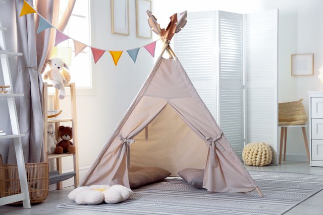 A fabric play tent and cushions sit among children's furniture and toys in a light-colored room.