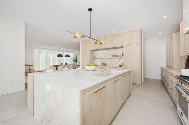 Light timber cabinetry, a pale stone island and warm metal fixtures create a bright open kitchen.