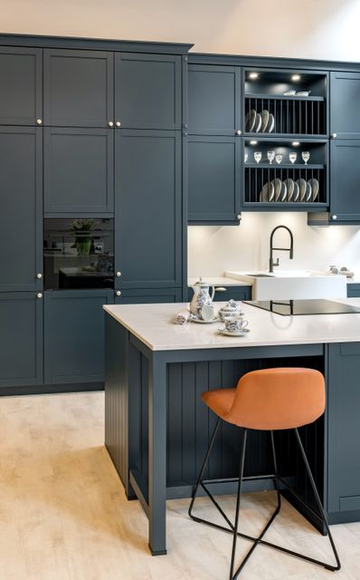 Dark grey cabinets and a pale island countertop are paired with an orange stool in a compact kitchen.