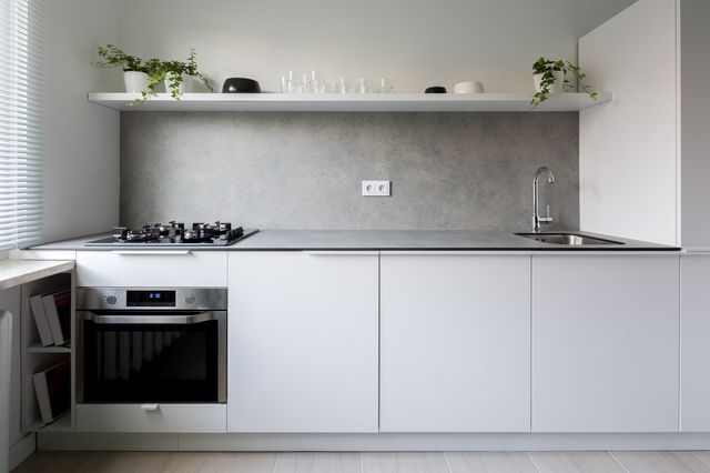 White cabinet fronts, a grey worktop and an open shelf create a clean, compact kitchen arrangement.