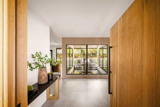 Wood-paneled walls and a console lead toward large glass doors and a water feature beyond.